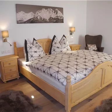 Ein gemütliches Schlafzimmer mit einem großen Holzbett und dekorativen Kissen. An den Wänden hängen Bilder und es gibt Nachttische neben dem Bett.