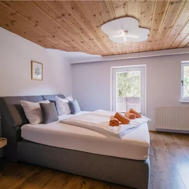 Ein modernes Schlafzimmer mit einem großen, bequemen Bett und neutralen Farben. Die Fenster lassen viel Tageslicht herein und sorgen für eine einladende Atmosphäre.