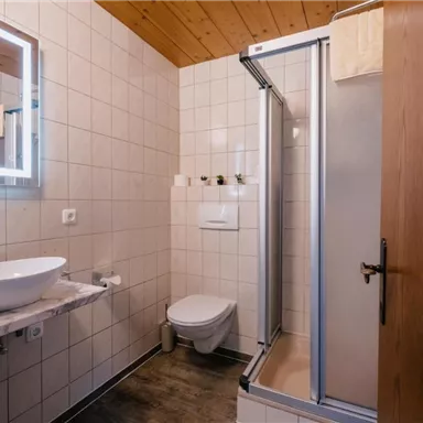 Ein modernes Badezimmer mit einer Dusche, einem Waschbecken und einer stilvollen Holzdecke. Die Wände sind mit weißen Fliesen verkleidet, und es gibt eine attraktive Beleuchtung.