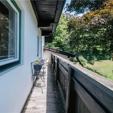 Ein schöner Balkon mit bequemen Stühlen und einem Tisch. Im Hintergrund ist eine grüne Wiese und Bäume zu sehen.
