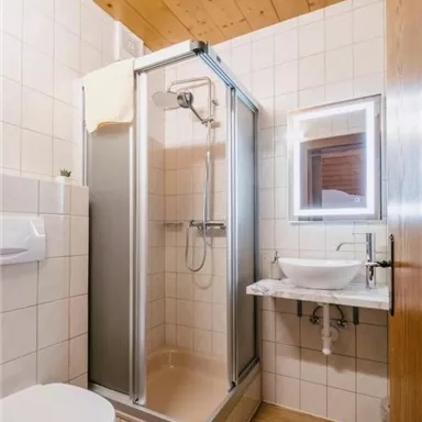 Ein modernes Badezimmer mit einer Dusche, einem Waschbecken und einer Toilette. Die Wände sind mit hellen Fliesen gefliest und der Boden ist aus Holz.