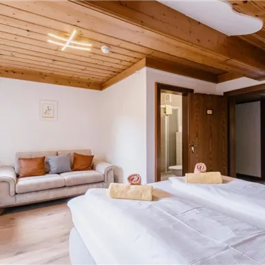 Ein helles und modernes Schlafzimmer mit zwei Einzelbetten und einer gemütlichen Couch. Die Holzwände und der Boden verleihen dem Raum eine warme Atmosphäre.