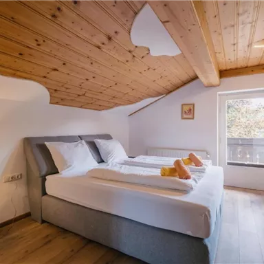 Ein gemütliches Schlafzimmer mit Holzpaneelen und zwei Betten. Die große Fensterfront lässt viel Tageslicht herein und bietet einen Blick nach draußen.