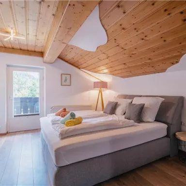 Ein gemütliches Schlafzimmer mit einer Holzdecke und einem großen Bett. Es gibt einen Fensterblick auf einen kleinen Balkon und dekorative Handtücher auf dem Bett.