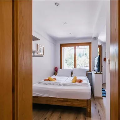 Ein gemütliches Schlafzimmer mit einem Doppelbett und hellen Fenstern. Der Raum hat Holzdetails und eine warme Atmosphäre.