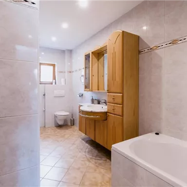 Ein modernes Badezimmer mit hellen Fliesen und Holzmöbeln. Es gibt eine Badewanne, ein Waschbecken und eine Toilette.