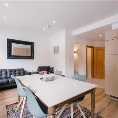 Ein modernes Wohnzimmer mit einem Essbereich und einer eleganten Küche. Die Wände sind hell und es gibt viel natürliches Licht.