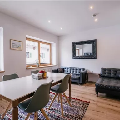 Ein heller Wohnraum mit einem Esstisch und bequemen Sofas. Die großen Fenster bieten viel Tageslicht und einen Blick nach draußen.