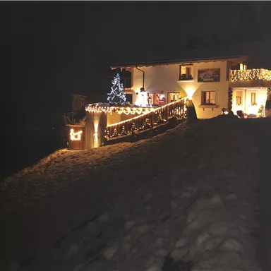 Ein schön beleuchtetes Haus im Schnee. Weihnachtslichter und ein geschmückter Baum schaffen eine festliche Stimmung.