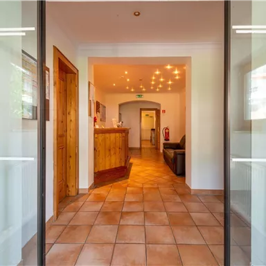 Ein einladender Empfangsbereich mit Holztresen und warmem Licht. Der Boden ist gefliest und die Wände sind hell gestrichen.