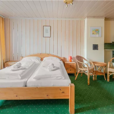 Ein gemütliches Schlafzimmer mit zwei Einzelbetten und heller Holzdecke. Der Raum ist mit einem Tisch, Stühlen und Teppich in grünem Farbton ausgestattet.