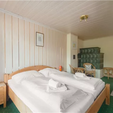 Ein gemütliches Schlafzimmer mit einem großen Doppelbett und Holzmöbeln. Die Wände sind hell und der Boden ist mit grünem Teppich ausgelegt.