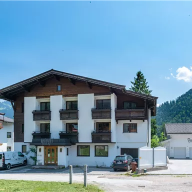 Ein gemütliches Haus in den Bergen mit traditionellen Balkonen und einem klaren blauen Himmel. Die Umgebung ist ruhig und einladend.