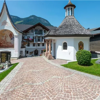 Eine malerische Straße mit gepflastertem Boden und traditioneller Architektur. Im Hintergrund sind Berge und blauer Himmel zu sehen.