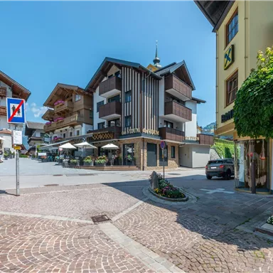Ein malerisches Dorf mit modernen und traditionellen Gebäuden. Auf der Straße stehen Tische und Stühle für Gäste.