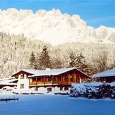 A picturesque winter landscape with snow-covered mountains in the background. In the foreground, cozy wooden houses stand in a calm, snowy environment.