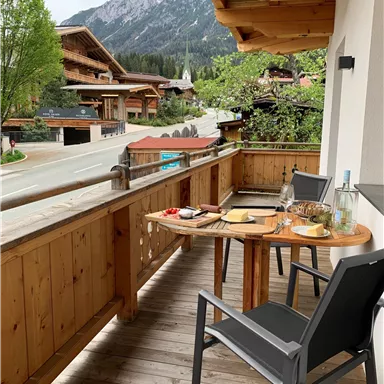 A cozy balcony with wooden furniture and a view of the mountains. Snacks and drinks are on the table.