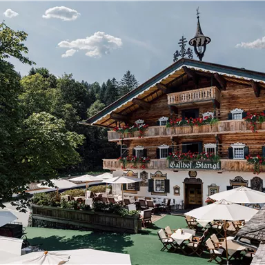 A traditional chalet with a wooden facade and colorful flowers. The outdoor area features cozy seating areas and sunshades.