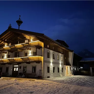Ein charmantes, beleuchtetes Gebäude im Alpinstil bei Nacht. Der Schnee schafft eine ruhige Winteratmosphäre.