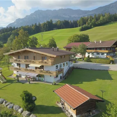 A beautiful building in a rural setting with green meadows and mountains in the background. In the foreground, there is a wooden playground.