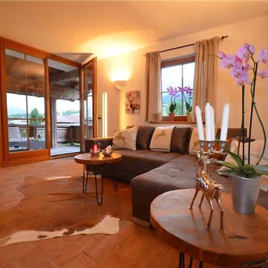 A modern living room with a comfortable couch and wooden tables. Large windows let in plenty of light and offer a view of the surroundings.