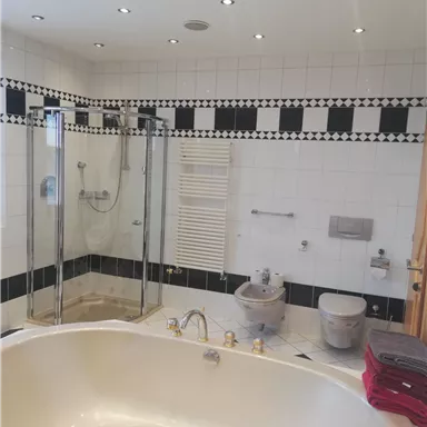 A modern bathroom with a bathtub and a glass shower. The walls are decorated with white tiles and a black-and-white border.