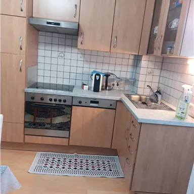 A modern kitchen with wooden cabinets and a bright color scheme. It is well equipped with a stove, sink, and various kitchen utensils.
