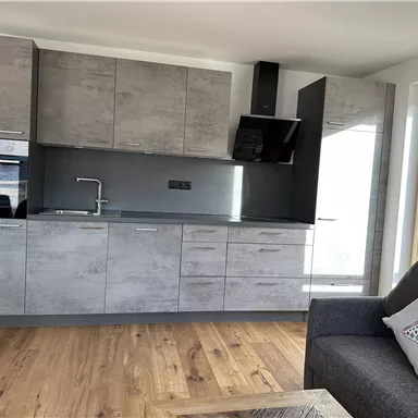 Eine moderne Küche mit grauen Möbeln und Holzfußboden. Es gibt einen Herd, eine Spüle und viel Stauraum.