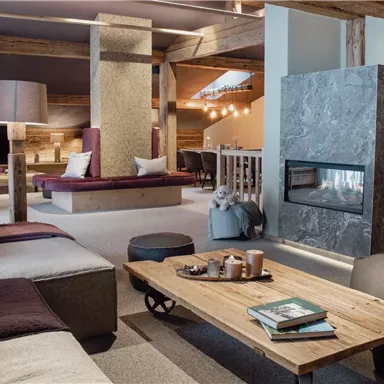 Ein modernes Wohnzimmer mit einer gemütlichen Sitzgruppe und einem Kamin. Die Holzelemente und die warmen Farben schaffen eine einladende Atmosphäre.