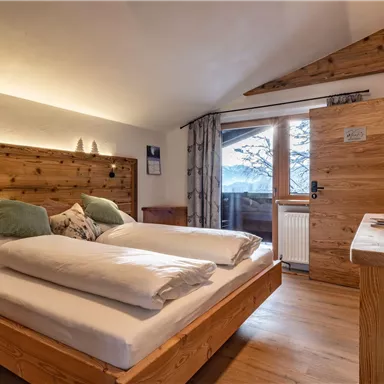 Ein gemütliches Schlafzimmer mit Holzdekor und einem bequemen Doppelbett. Die großen Fenster bieten einen Blick auf die verschneite Landschaft.