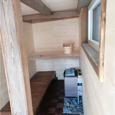 Ein gemütlicher Sauna-Raum mit Holzregalen und einem Holzofen. Der Boden ist mit Holzplanken und Steinen gestaltet.