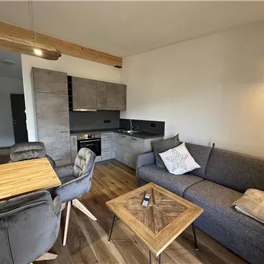 Eine moderne Wohnung mit einer gemütlichen Sitzecke und einem Esstisch. Die Küchenzeile ist gut ausgestattet und der Boden ist aus Holz.