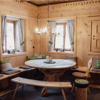 Ein gemütlicher Raum mit Holzvertäfelungen und einer runden Tischgruppe. Bänke und Kissen laden zum Verweilen ein.