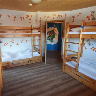 Ein gemütlicher Schlafsaal mit Stockbetten aus Holz. Die Wände sind mit bunten Musiknoten dekoriert.