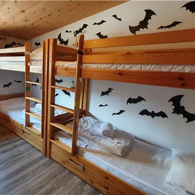 Ein gemütlicher Schlafraum mit Etagenbetten aus Holz. Die Wände sind mit fliegenden Fledermäusen dekoriert.