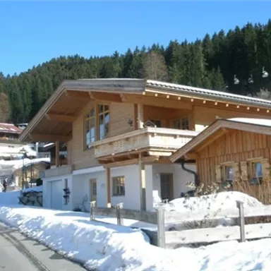 A beautiful wooden house in a snow-covered landscape. In the background, snow-capped mountains and coniferous trees can be seen.