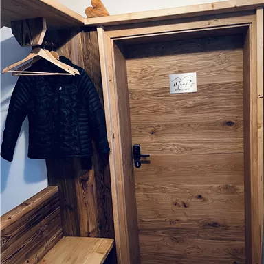 Ein gemütlicher Eingangsbereich mit einer Holzbank, einem hängenden Mantel und einer Holztür. Der Raum hat rustikale Elemente und eine warme Atmosphäre.
