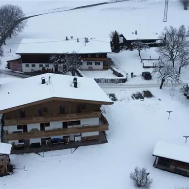A wintry landscape with several houses covered in snow. The sky is gray and the surroundings appear calm and peaceful.