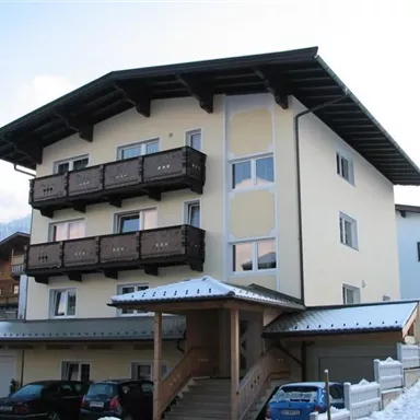 Ein modernes Gebäude mit drei Etagen und Balkonen aus Holz. Die Umgebung ist winterlich mit Schnee bedeckt.