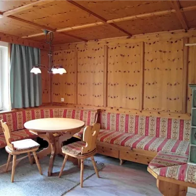 Ein gemütlicher Raum mit Holzwänden und einer Sitzecke. Ein runder Tisch ist von gepolsterten Bänken umgeben.