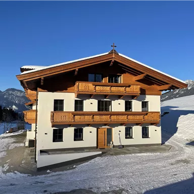 A modern chalet in alpine style, surrounded by snow. The clear blue sky complements the picturesque landscape.