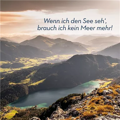 An impressive mountain landscape with a clear lake in the foreground. The surrounding hills and mountains are softly illuminated by the evening sun.