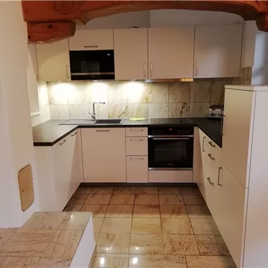 A modern kitchen with white cabinets and electrical appliances. The room has bright lighting and an elegant flooring.