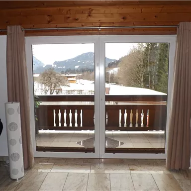 A spacious room with large windows and a view of a snow-covered landscape. The surroundings are characterized by mountains and trees.