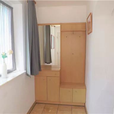 A bright entrance area with a wooden cabinet and a coat rack. The window lets in plenty of daylight.