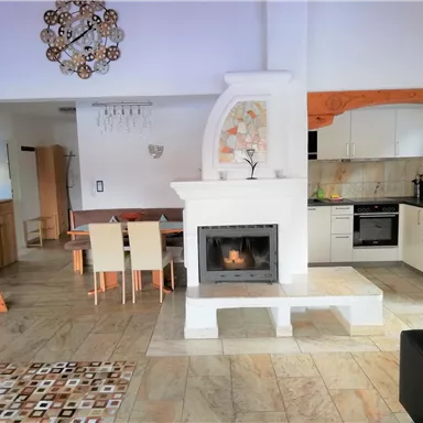 A modern living space with a bright kitchen and a cozy fireplace. The room has a friendly atmosphere and warm wooden details.