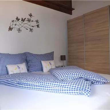 A cozy bedroom with a large bed and checkered pillows. In the background, there is a modern wooden wardrobe.