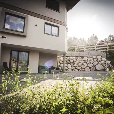 A modern house with a sunny outdoor area and a tastefully designed garden. The walls are light, and the windows offer a view of the surroundings.