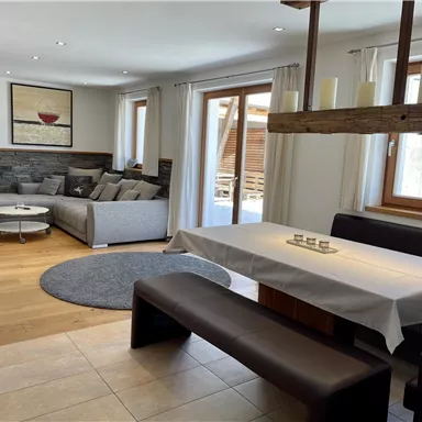 Ein modernes Wohnzimmer mit einem gemütlichen Sofa und einem Esstisch. Große Fenster sorgen für viel Tageslicht und eine einladende Atmosphäre.