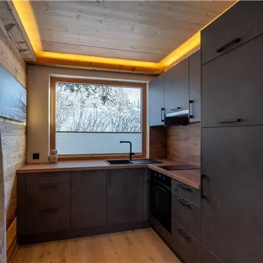 Eine moderne Küche mit Holzverkleidung und einem großen Fenster. Die Ausstattung ist funktional und stylish mit einer sanften Beleuchtung.